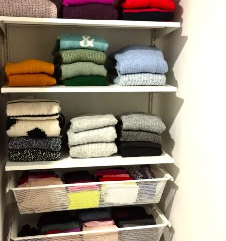 Jerséis doblados por color en la estantería de un vestidor organizado